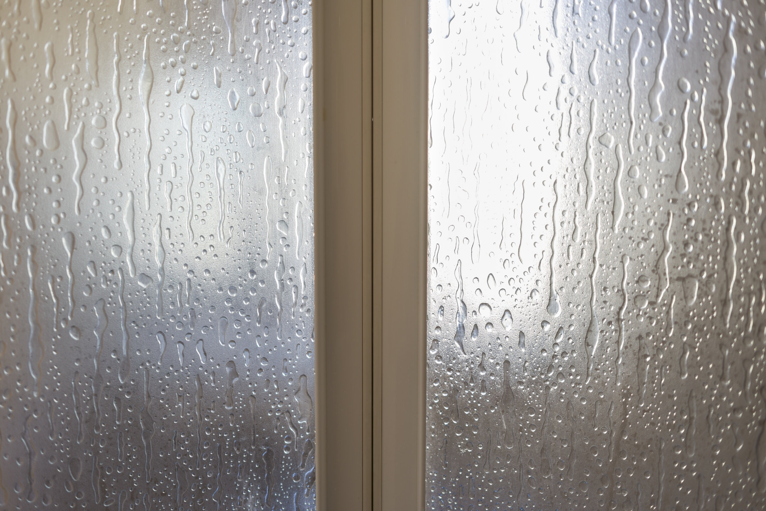 Dettaglio di vetri con condensa di una finestra a due ante bianche vista dall'interno di un'abitazione